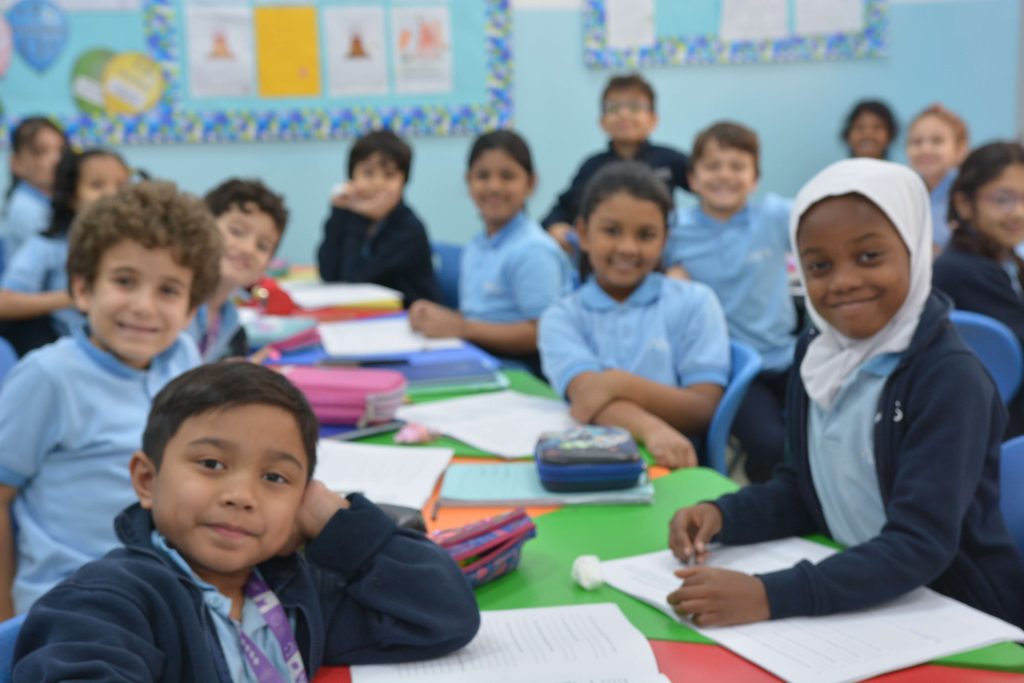 ANPS Primary students seated along a long classroom table with coloured paper and pencil cases, working together