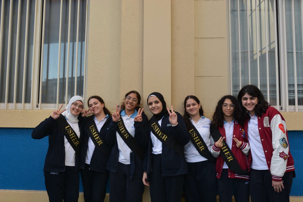 ANPS Middle School students in navy uniform wearing named sashes posing together in a corridor
